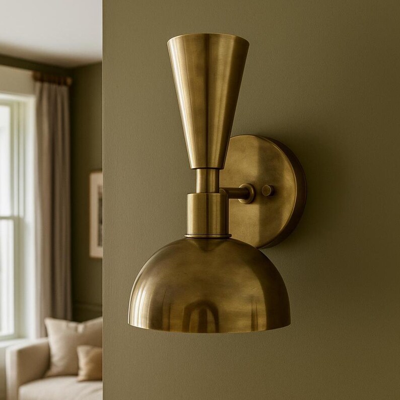 May include: A brass wall sconce with a conical top and a rounded, dome-shaped bottom. The fixture is mounted on a circular backplate and has a warm, metallic finish. The sconce is designed for indoor lighting.
