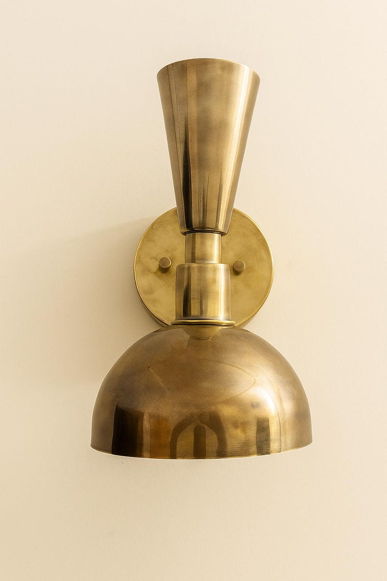 May include: A brass wall sconce with a conical top and a rounded, dome-shaped bottom. The sconce is mounted on a circular backplate and has a warm, metallic finish. The design is a vintage style.