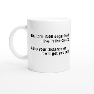 May include: White ceramic mug with a curved handle. The mug features black text that reads: "No, I am NOT organised, I live in the CHAOS. Keep your distance or it will get you too!"