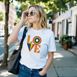 Könnte beinhalten: Weißes T-Shirt mit dem Wort "LOVE" in Orange und Regenbogenfarben. Das "O" in LOVE ist ein Regenbogenkreis. Das Shirt wird mit blauen Jeans und Sonnenbrille getragen.