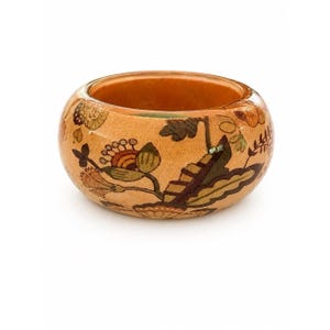 May include: A wide, rounded bangle bracelet featuring a light tan base color with a detailed floral and botanical pattern in shades of brown, orange, green, and cream. The surface has a smooth, polished finish with a visible wood-like texture.