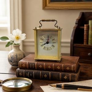 May include: A rectangular brass carriage clock with a silver face, black Roman numerals, and a top handle. The clock features the word Dawn printed in black above the center hands and the word Quartz below, with the word Alarm at the bottom.