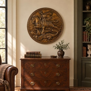 May include: A circular bronze-toned wall plaque featuring a high-relief sculpture of a knight on horseback battling a dragon. The plaque has a detailed border and is mounted on a wall above a dark wooden chest of drawers with three drawers.