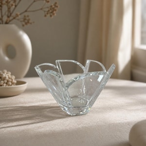 May include: A clear glass bowl featuring a distinct petal-like design with six curved, upright segments that flare outward from a central base. The transparent glass has smooth, rounded edges and a polished finish, creating a flower-shaped silhouette.