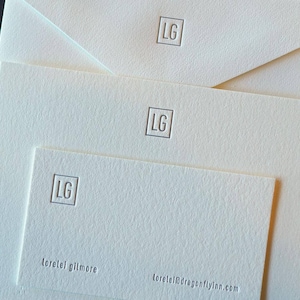 May include: A stack of white stationery with a simple, embossed "LG" logo and the text "lorelei gilmore" and "loreleigilmoreflynn.com".