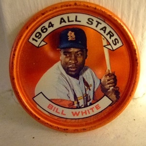 Peut inclure: Un jeton rond en métal orange avec une image blanche d'un joueur de baseball portant une casquette de baseball et tenant une batte. Le texte "1964 ALL STARS BILL WHITE" est imprimé sur le jeton.