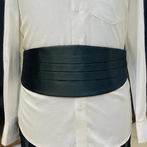 May include: A formal wear ensemble on a mannequin. It features a white textured dress shirt, a black bow tie, and a black cummerbund. The shirt has long sleeves and a chest pocket. The cummerbund is pleated.