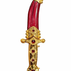 May include: An ornate dagger with a curved, red blade. The hilt and decorative elements are gold-colored, featuring intricate floral designs and red gemstone accents. A small red tassel hangs from the base.