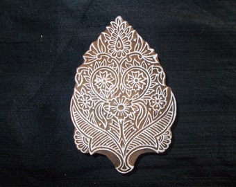 May include: A white wooden block with a carved design of a floral pattern. The design is intricate and detailed, with leaves, flowers, and swirls.