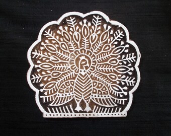 May include: A white wooden block printing stamp with a detailed design of a peacock with its tail feathers spread out. The design is in brown and white.