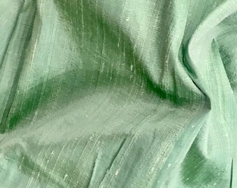 May include: A close-up of a soft, green fabric with a subtle sheen. The fabric has a woven texture and is slightly wrinkled.