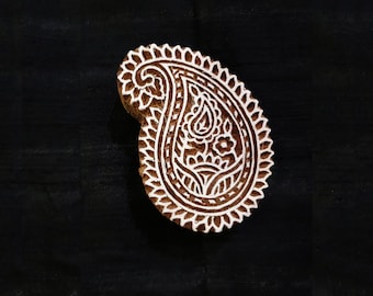 May include: A wooden block printing stamp with a detailed paisley design. The stamp is carved with a intricate pattern of leaves, flowers, and swirls.