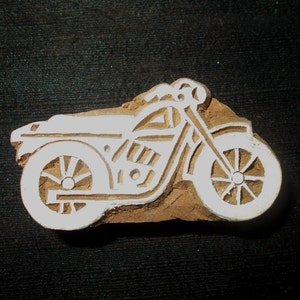 Peut inclure: Une gravure sur bois d'une moto, avec de la peinture blanche délimitant le dessin. La moto a deux roues et un design détaillé.