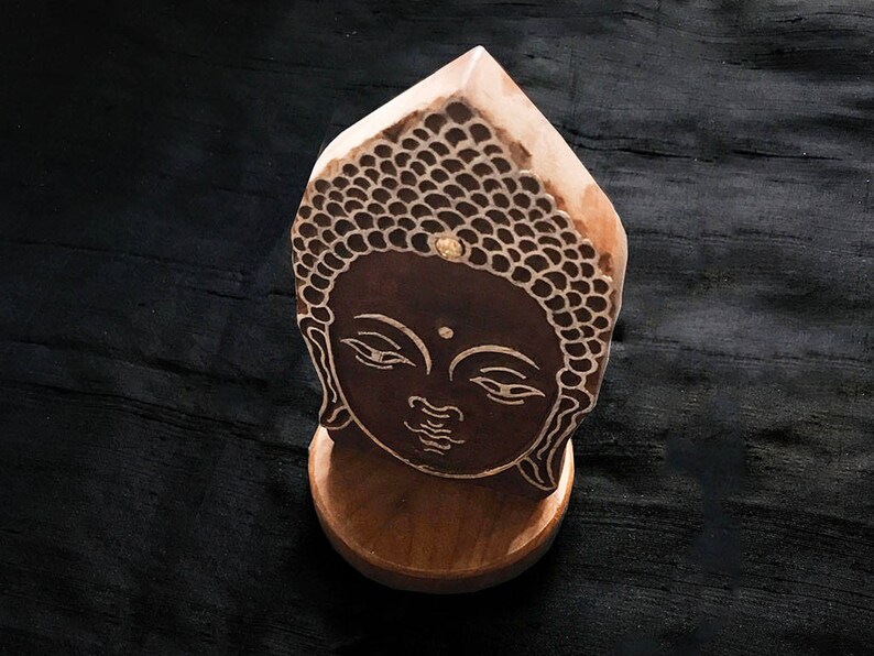May include: A wooden sculpture of a Buddha's face with a brown and black design. The sculpture is on a wooden base.