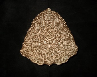 May include: A white wooden block with a detailed paisley design carved into it. The block is used for printing patterns onto fabric.