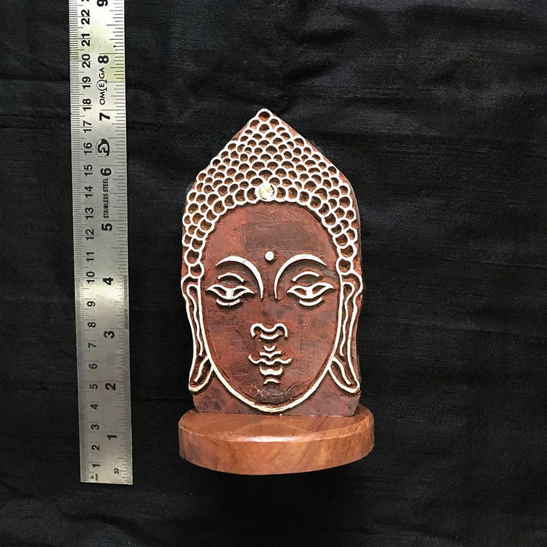 May include: A wooden carving of a Buddha head with a white design, mounted on a wooden base.