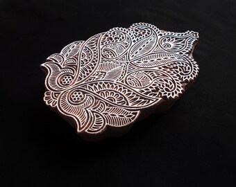 May include: A wooden block printing stamp with a detailed paisley design. The stamp is carved with intricate floral patterns and swirls.