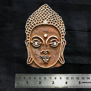 May include: A wooden block carving of the face of Buddha. The carving is detailed and shows the face of Buddha with a serene expression. The carving is approximately 5 cm wide.