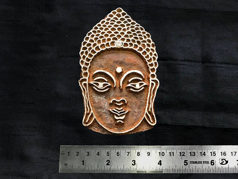 May include: A wooden block carving of the face of Buddha. The carving is detailed and shows the face of Buddha with a serene expression. The carving is approximately 5 cm wide.