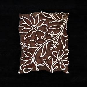 Puede incluir: Un bloque de madera marrón con un diseño floral blanco. El diseño presenta una flor grande con una flor más pequeña y hojas.