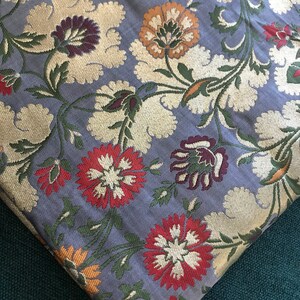 May include: A close-up of a grey fabric with a floral pattern. The flowers are red, white, orange, and green. The fabric has a metallic sheen.