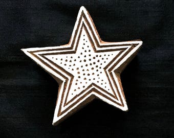 May include: A white wooden star-shaped printing block with a dotted pattern inside the star. The block is on a black background.