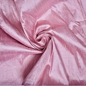 May include: A piece of light pink fabric with a subtle, iridescent sheen and a visible slubbed texture. The material is gathered in the centre, creating soft, flowing folds and deep shadows that highlight the reflective quality of the textile.