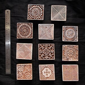 Puede incluir: Una colecci&oacute;n de once bloques de impresi&oacute;n cuadrados de madera con intrincados dise&ntilde;os tallados. Los bloques presentan patrones geom&eacute;tricos y florales en tonos marrones. Una regla con medidas en cent&iacute;metros es visible a la izquierda.