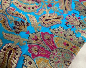 Könnte beinhalten: Nahaufnahme eines türkisfarbenen Stoffes mit Paisley-Muster. Der Stoff ist mit goldenen, braunen und rosafarbenen Fäden gewebt.