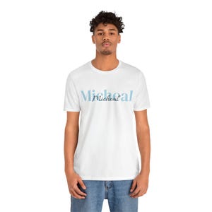 Può includere: Una t-shirt bianca a maniche corte con girocollo, caratterizzata dalla scritta "Micheal" stampata in un grande carattere serif azzurro sul petto, con il nome "Micheal" scritto anche in un carattere corsivo più piccolo di colore blu scuro.