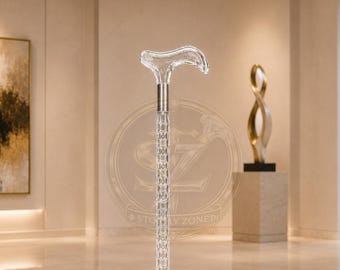 May include: A clear, transparent walking cane featuring a curved handle and a textured, diamond-patterned shaft. The cane includes a metallic silver-toned collar connecting the handle to the shaft and a black rubber tip at the base for stability.