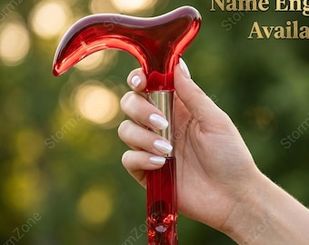 May include: A red acrylic cane with a curved handle and a decorative shaft. The cane is held in a hand against a blurred green background. Text on the image reads "Name Engraving Available".