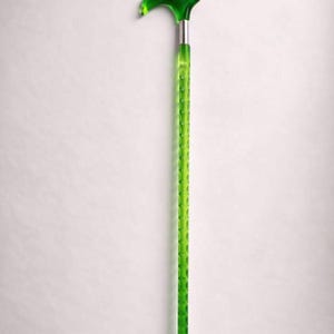 May include: A green walking cane with a curved handle and a textured shaft. The handle and the top of the shaft are a darker shade of green, while the shaft has a lighter green color. The cane has a silver metal band and a silver tip.