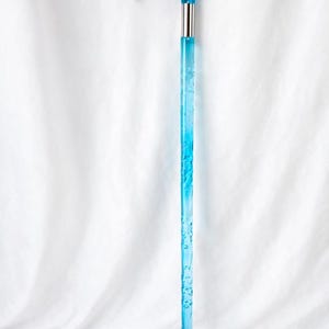 May include: A transparent blue walking cane with a curved handle. The handle and shaft are a vibrant blue color, with a silver metal band connecting the handle to the shaft. The shaft has a decorative pattern.