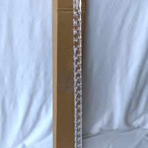 May include: A clear acrylic walking cane with a curved handle and a decorative, faceted shaft. The cane is approximately 36 inches long and has a silver-colored metal band at the top and bottom. It is positioned next to a brown cardboard box.