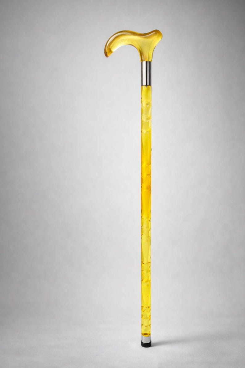 May include: A transparent yellow walking cane with a curved handle. The cane has a silver metal band near the top and bottom. The shaft has a textured, bubbly appearance. The cane is a stylish mobility aid.