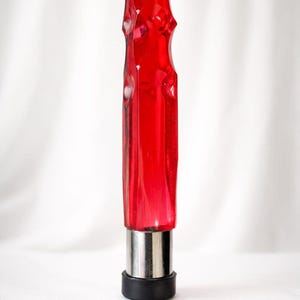 May include: A red, faceted glass object with a silver base and a black rubber tip. The object has a textured, ridged design. The background is a plain white.