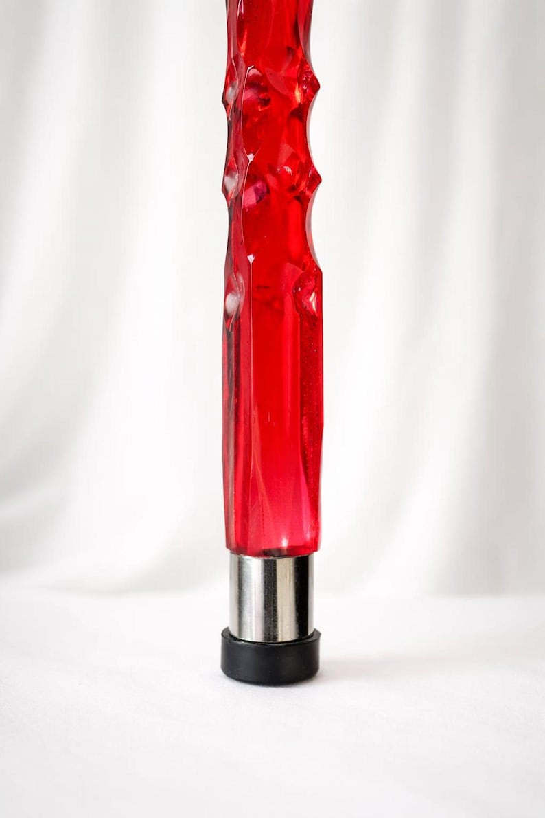 May include: A red, faceted glass object with a silver base and a black rubber tip. The object has a textured, ridged design. The background is a plain white.