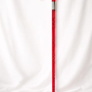 May include: A vibrant red walking cane with a curved handle and a silver metal band. The shaft features a series of small, decorative indentations. The cane is designed for support and mobility.
