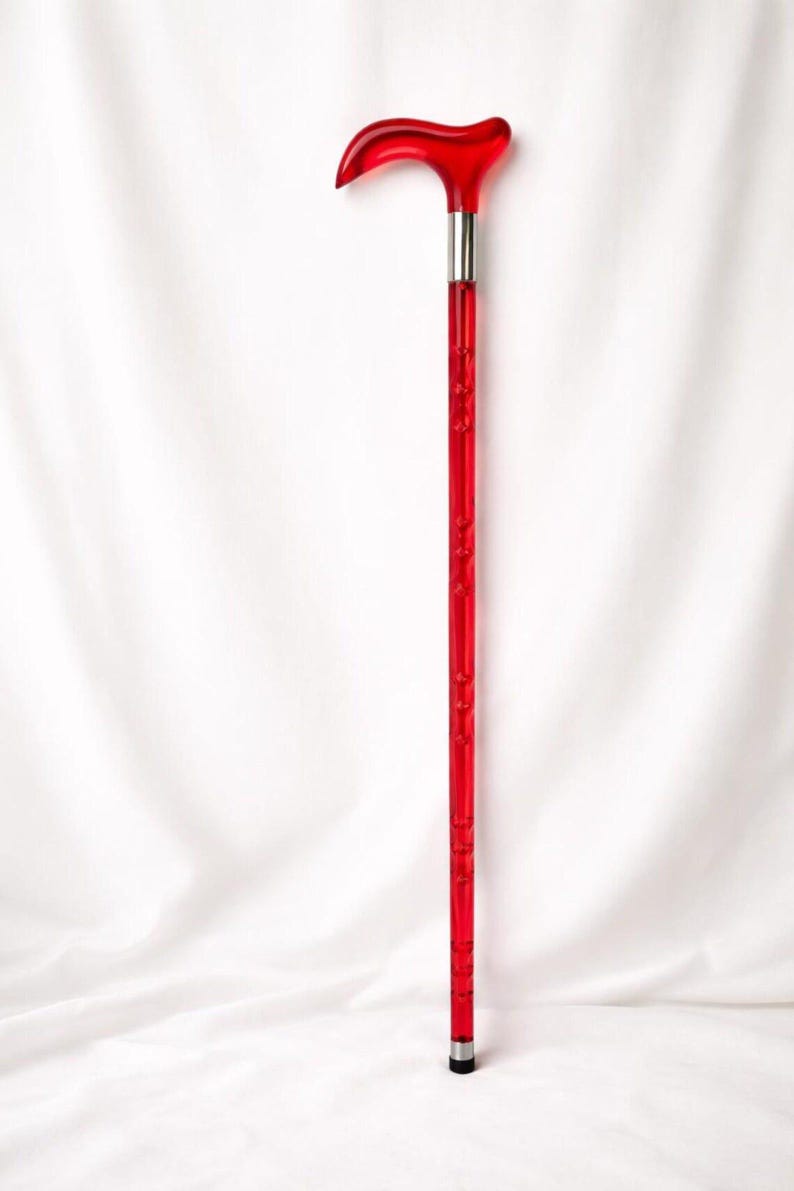 May include: A vibrant red walking cane with a curved handle and a silver metal band. The shaft features a series of small, decorative indentations. The cane is designed for support and mobility.