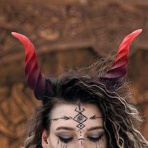 May include: A pair of spiraled, curved horns featuring a gradient color transition from deep black at the base to a vibrant red at the tips. The horns are positioned atop the head, displaying a textured, ridged surface throughout their length.