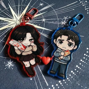 May include: Two acrylic keyrings with cartoon characters, one red and one blue. The red keyring shows a girl holding a card that says "ONE WISH WILLOW". The blue keyring depicts a boy holding a similar card. They are linked by a red heart.