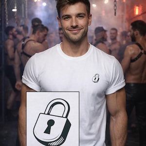 May include: A white t-shirt featuring a small black and white padlock design. The t-shirt is worn by a person smiling. The background is blurred, with other people visible.