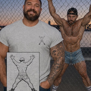 以下が含まれることがあります： 腕を上げた人の小さな白黒グラフィックが付いた、明るい灰色のTシャツ。画像には、デニムショーツと黒いキャップを着用し、金網のフェンスに寄りかかっている人も写っています。