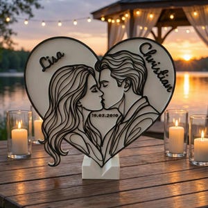 Könnte beinhalten: Herzförmige Holzdekoration mit einer Silhouette eines sich küssenden Paares, mit den Namen "Lisa" und "Christian" eingraviert. Das Datum "19.03.2010" ist ebenfalls vorhanden. Die Dekoration ist weiß und schwarz und steht auf einem weißen Sockel. Kerzen und ein Pavillon sind im Hintergrund.
