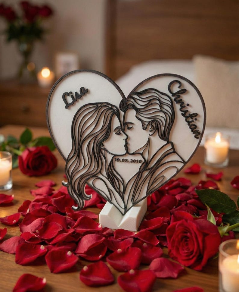 Puede incluir: Una escultura de madera en forma de coraz&oacute;n que representa a una pareja bes&aacute;ndose, con los nombres "Lisa" y "Christian" y la fecha "19.03.2010" inscritos. La escultura est&aacute; sobre una base blanca, rodeada de p&eacute;talos de rosas rojas y velas.
