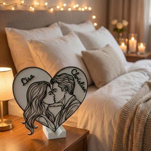 Puede incluir: Luz de noche en forma de coraz&oacute;n de madera, con la silueta de una pareja bes&aacute;ndose. Los nombres "Lisa" y "Christian" est&aacute;n inscritos, junto con la fecha "19.03.2019". La luz est&aacute; sobre una base blanca, en una mesita de noche de madera.