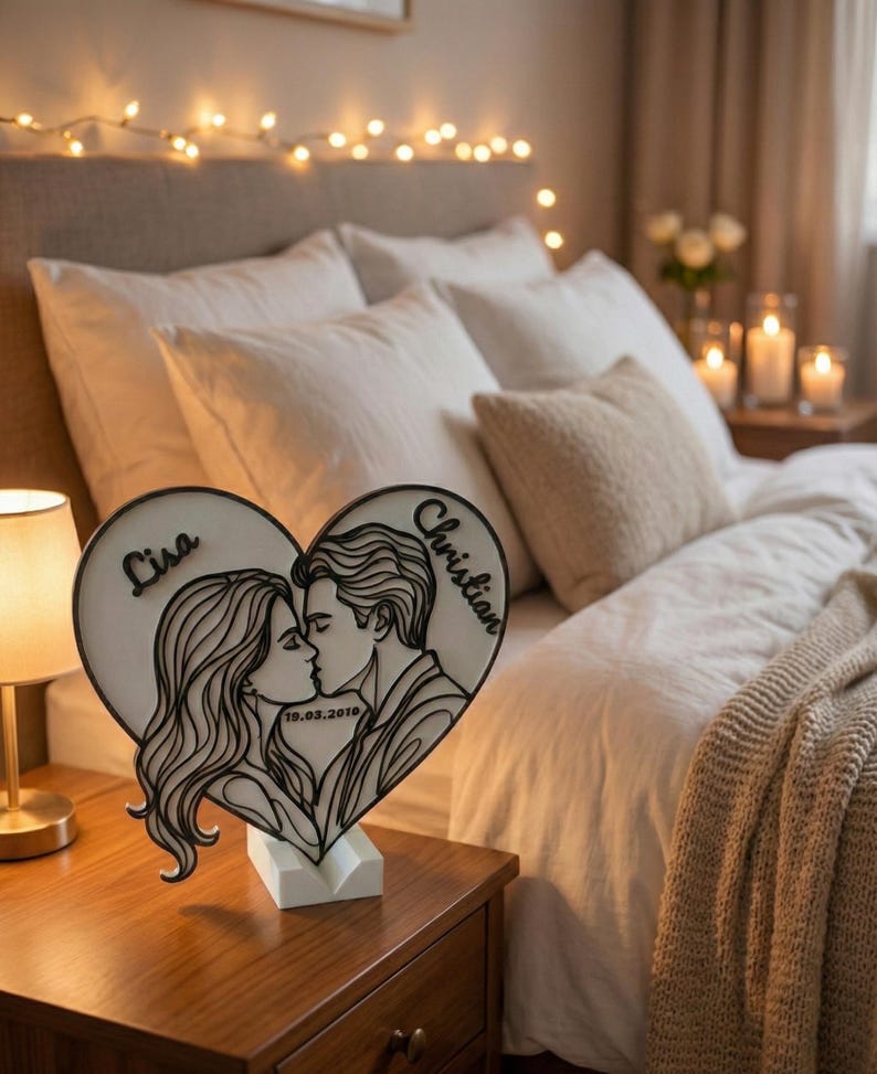 Puede incluir: Luz de noche en forma de coraz&oacute;n de madera, con la silueta de una pareja bes&aacute;ndose. Los nombres "Lisa" y "Christian" est&aacute;n inscritos, junto con la fecha "19.03.2019". La luz est&aacute; sobre una base blanca, en una mesita de noche de madera.