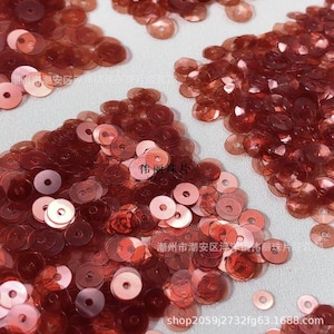 Op de afbeelding: Close-up van verspreide, roodbruine pailletten. De pailletten zijn cirkelvormig met een gat in het midden. De afbeelding bevat Chinese tekst en de website shop2059j2732fg63.1688.com.