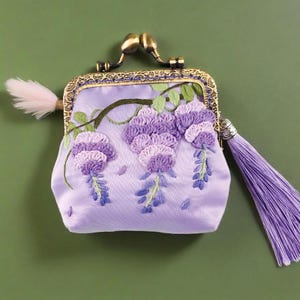 May include: A lavender satin coin purse with a brass clasp and a long tassel. The purse is embroidered with purple wisteria flowers and green leaves. A small, fluffy, pink feather is attached to the side.